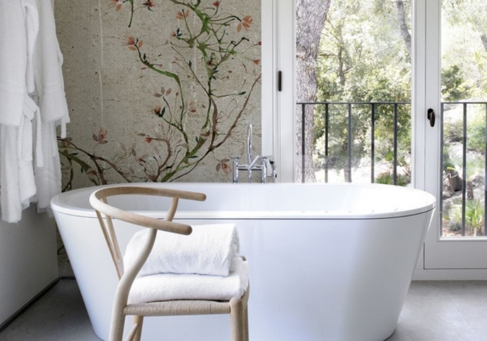 Freistehende Badewanne mit floraler Tapete und schlichten Fliesen in Beton-Optik, gestaltet vom Wohnatelier im Schlossquartier Eisenstadt – modernes Badezimmer mit Wellnesscharakter.