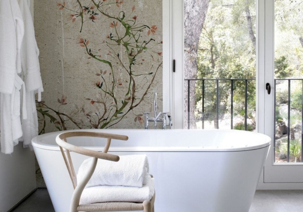 Freistehende Badewanne im Badezimmer mit Blumentapete und Holzstuhl – Wohnatelier im Schlossquartier in Eisenstadt